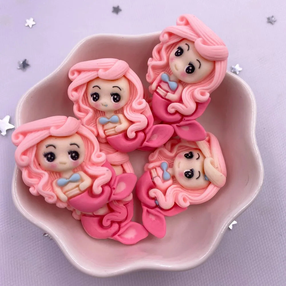 Pink resin figurines of mermaid princesses with curly hair and blue accents displayed in a pink dish.