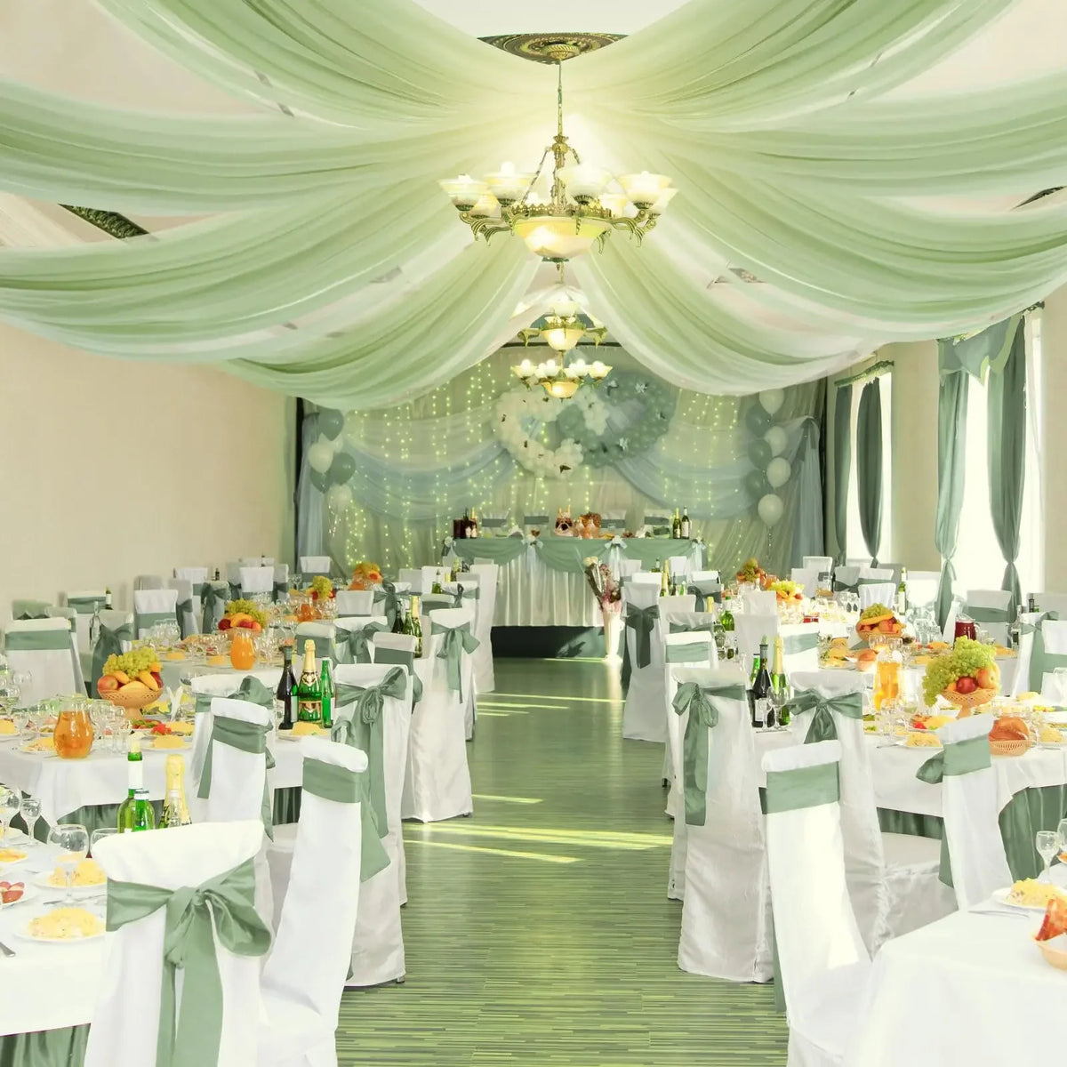 Elegant indoor event space decorated with sheer sage green chiffon curtains and white tables.