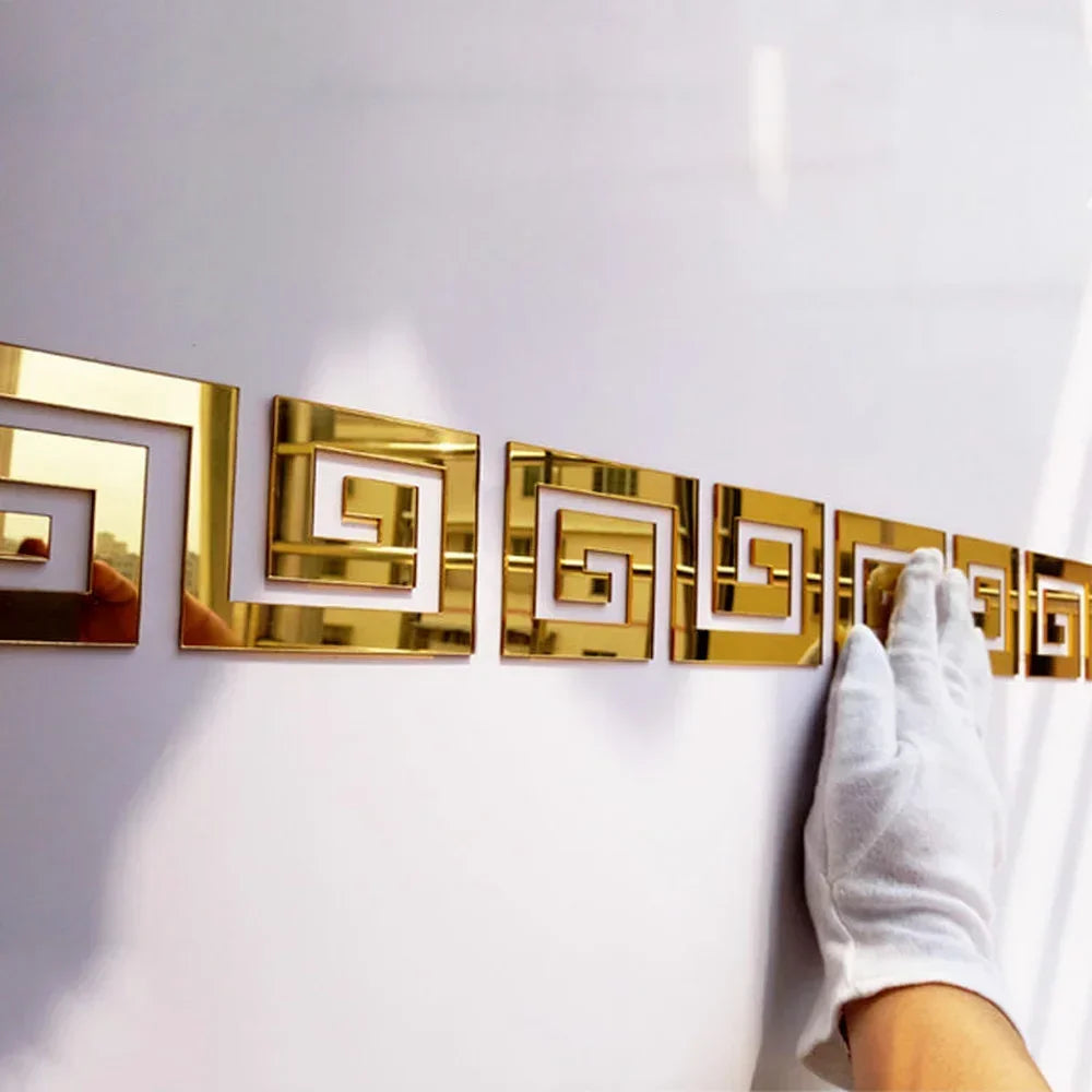 A row of gold acrylic mirror wall stickers in a Greek key pattern mounted on a white wall.