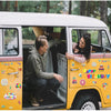 A woman is smiling while looking out of the open door of a yellow vintage van decorated with colorful birthday magnets.
