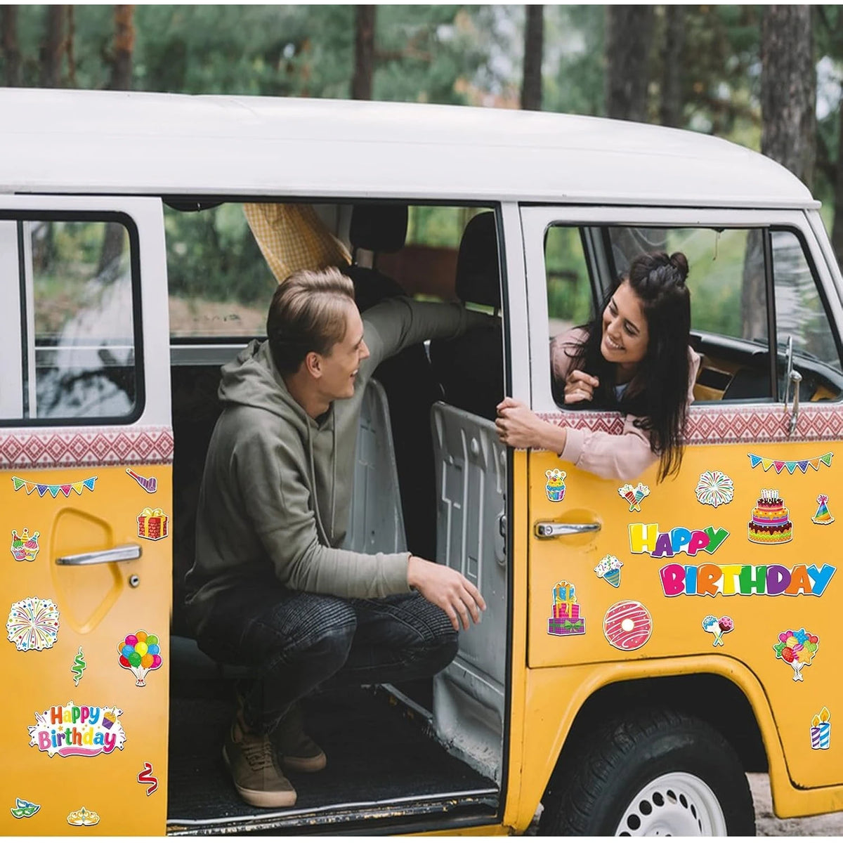 A woman is smiling while looking out of the open door of a yellow vintage van decorated with colorful birthday magnets.
