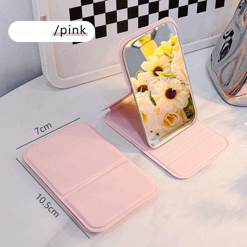 A pink portable folding HD makeup mirror with a floral design is shown next to its stand.