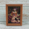 A framed painting featuring a black cat sitting on a path surrounded by lush greenery.