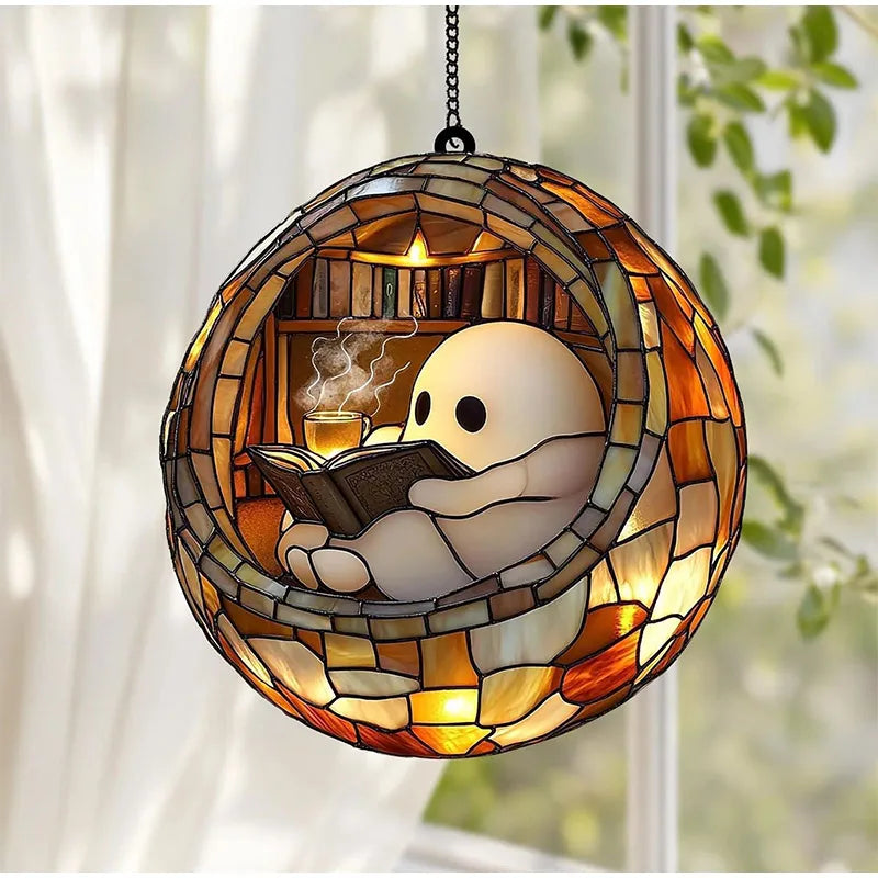 A stained glass hanging decoration shaped like a ghost reading a book inside a window frame.