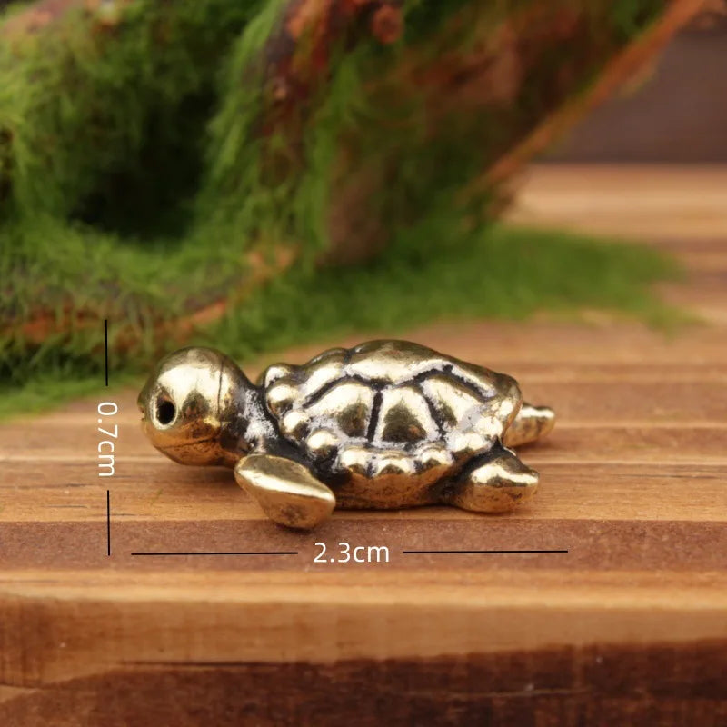A small brass turtle figurine resting on a wooden surface with moss in the background.
