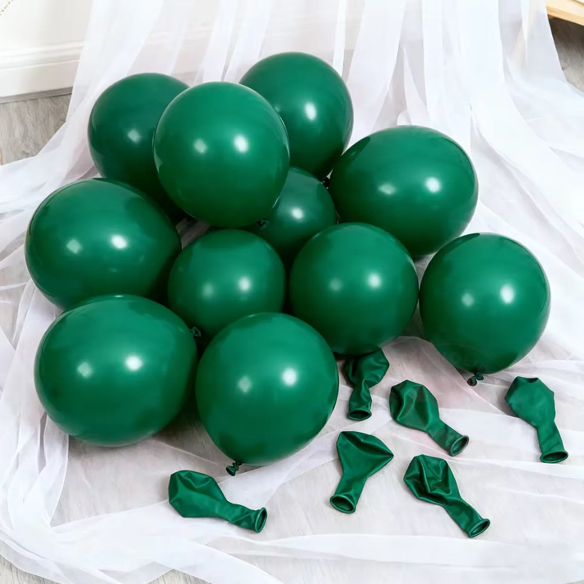 A cluster of dark green latex balloons scattered on white fabric.