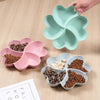 A light green heart-shaped four-compartment snack tray with various dry snacks inside.
