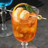 An orange-colored cocktail in a glass garnished with citrus slices and bamboo skewers.