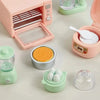 A pink kitchen appliance dollhouse set featuring a food processor, a citrus juicer, and various accessories like eggs and gra