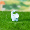 A small, light blue elephant figurine is placed on green grass with measurement lines.
