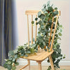 A wooden chair decorated with a lush green artificial eucalyptus wreath garland.