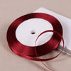 A roll of deep red satin ribbon on a white spool, lying on a light beige surface.