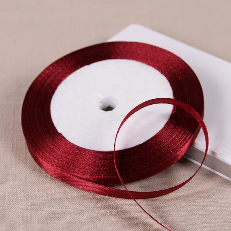 A roll of deep red satin ribbon on a white spool, lying on a light beige surface.