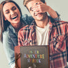 A young couple smiling while holding a handmade scrapbook album for memories and adventures.
