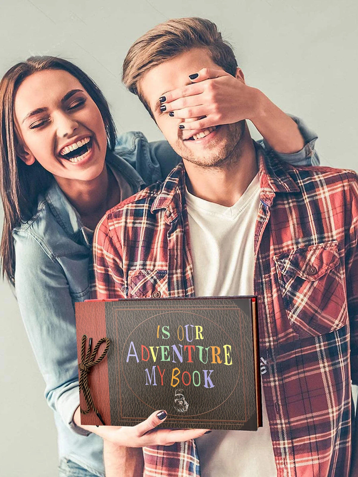A young couple smiling while holding a handmade scrapbook album for memories and adventures.