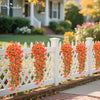 White picket fence decorated with bright orange artificial morning glory vines in a garden setting.