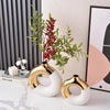 A display of luxury ceramic flower vases featuring gold and white finishes with green foliage.