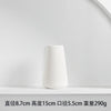 A white ceramic vase with a tapered shape is displayed on a white shelf.