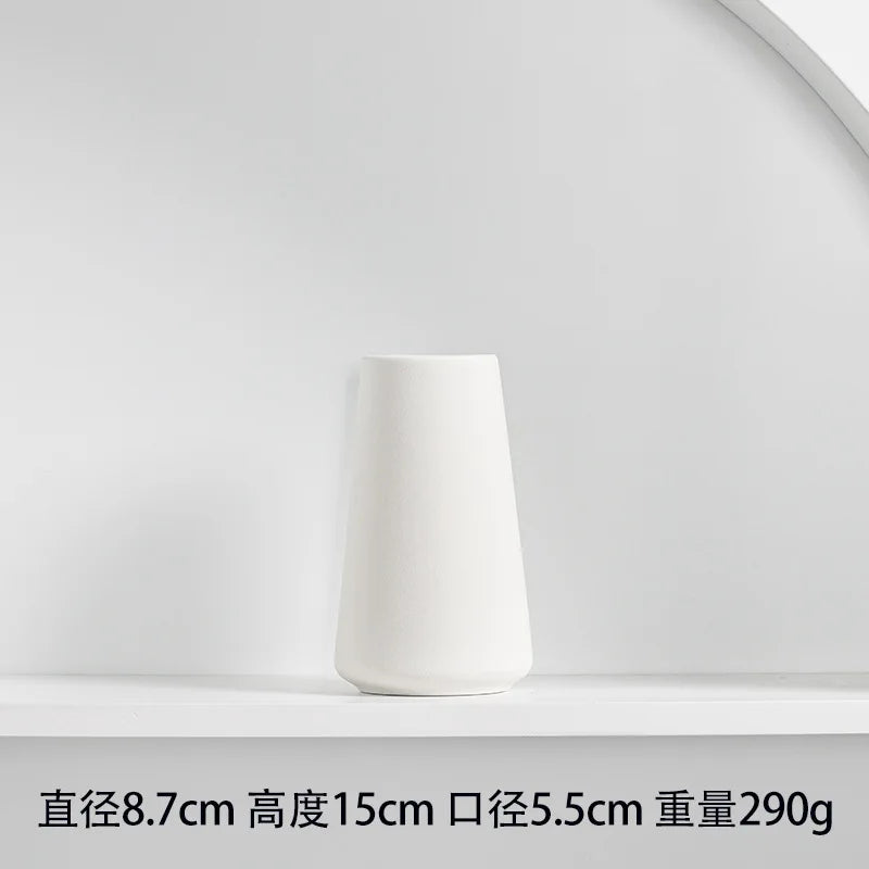 A white ceramic vase with a tapered shape is displayed on a white shelf.
