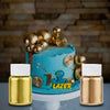 A cake decorated with gold and silver glitter dust next to two glass bottles of gold liquid.