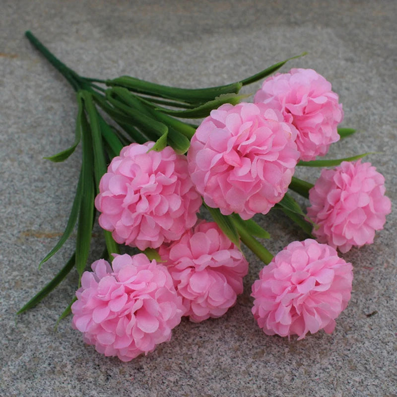 Un bouquet de fleurs artificielles d'hydrangea roses avec des tiges vertes sur une surface grise.
