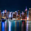 A nighttime view of the New York City skyline reflected on water.