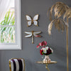 An artisan butterfly wall mirror with an antique gold frame mounted on a gray wall.