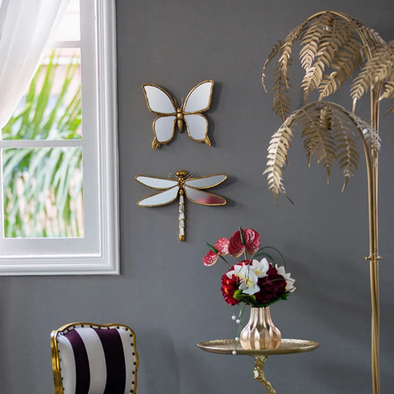 An artisan butterfly wall mirror with an antique gold frame mounted on a gray wall.