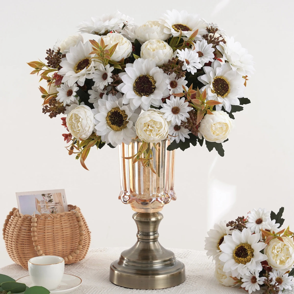 Un bouquet de fleurs artificielles blanches et crème, incluant des tournesols et des pivoines, dans un vase en verre.