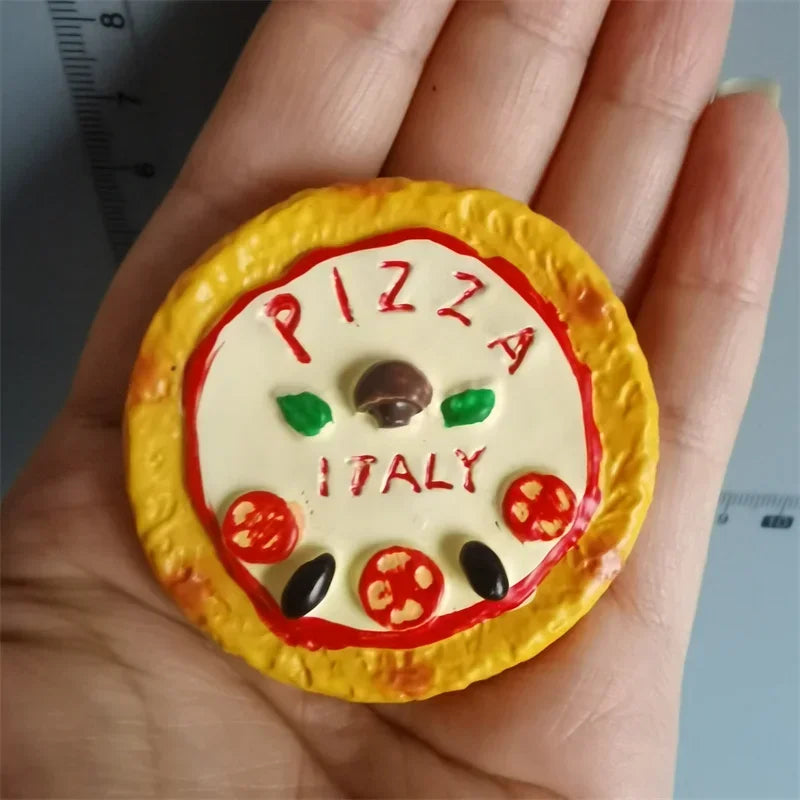A yellow food-shaped magnet featuring the word PIZZA and ITALY with tomato and olive decorations.