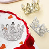 Mini gold and silver crown cake topper decorations with red rose petals on a white cake.