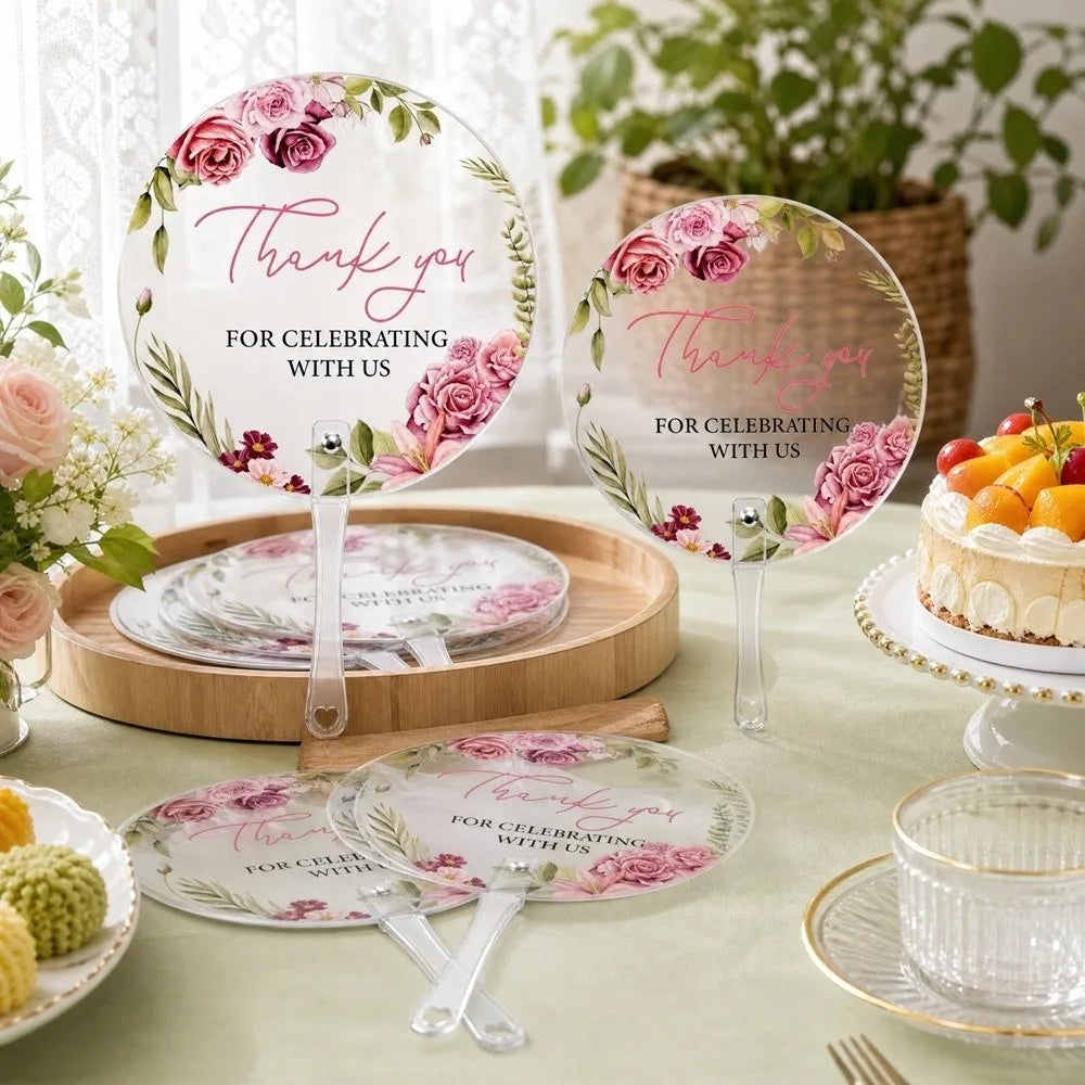 A set of pink floral thank you hand fans for celebrating with us displayed on a table.