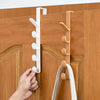 A hand is installing over-the-door hooks for bags, hats, and scarves onto a wooden door.