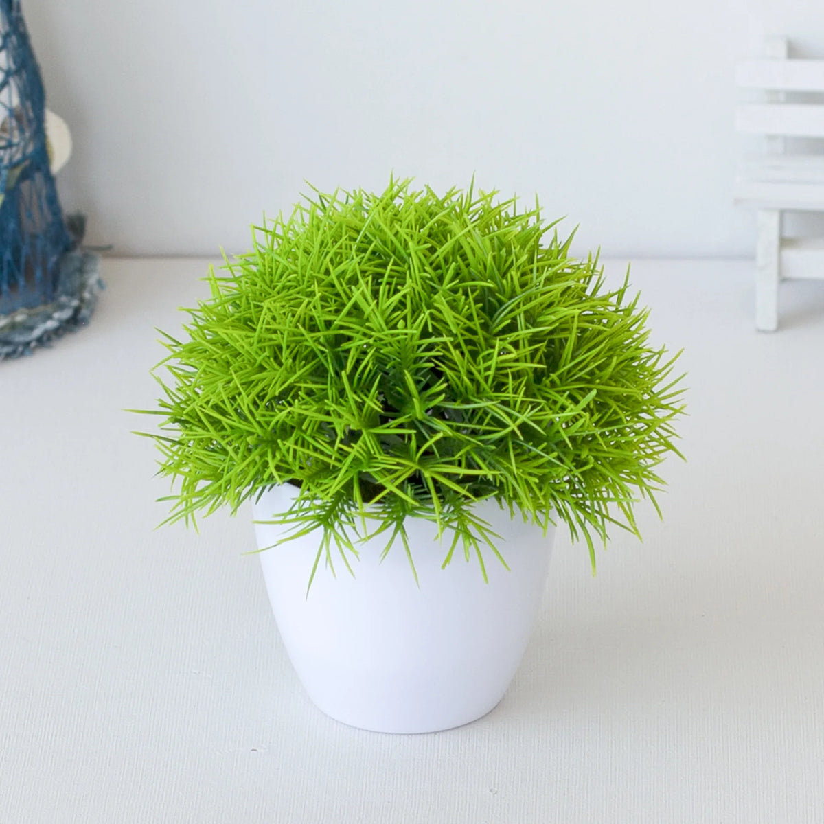 Un vibrant plant de bonsaï artificiel vert dans un pot blanc sur une surface blanche.