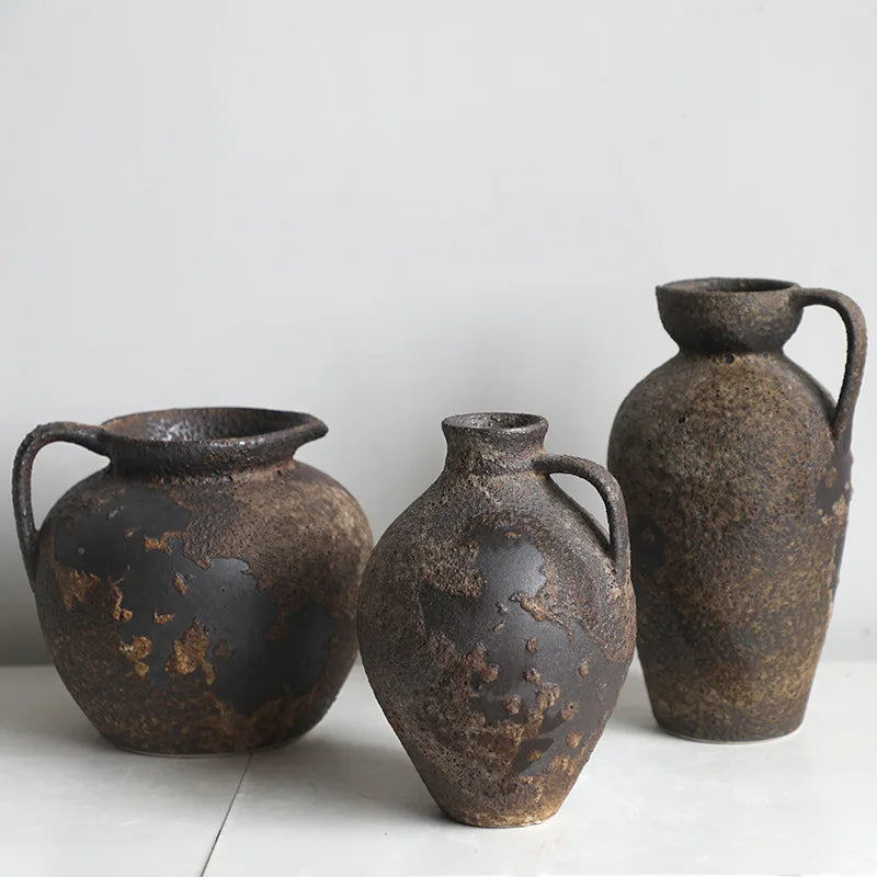A pair of dark, textured ceramic vases with handles and spouts, displayed against a white background.