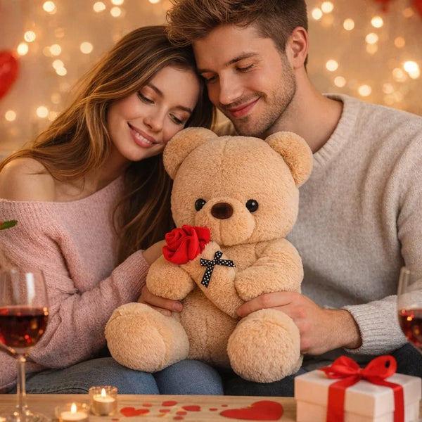 A woman and man are holding a rose bear plush toy in a cozy indoor setting.