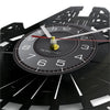 A close-up of a black vinyl record wall clock with a gold-colored pendulum and white markings.