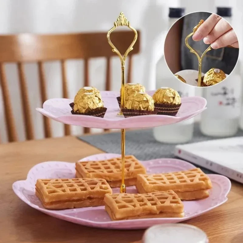 A gold-colored 3-tier cake stand holding small golden muffins and waffles on pink plates.
