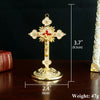 A gold-colored metal Jesus cross ornament with a decorative base, shown against a dark background.