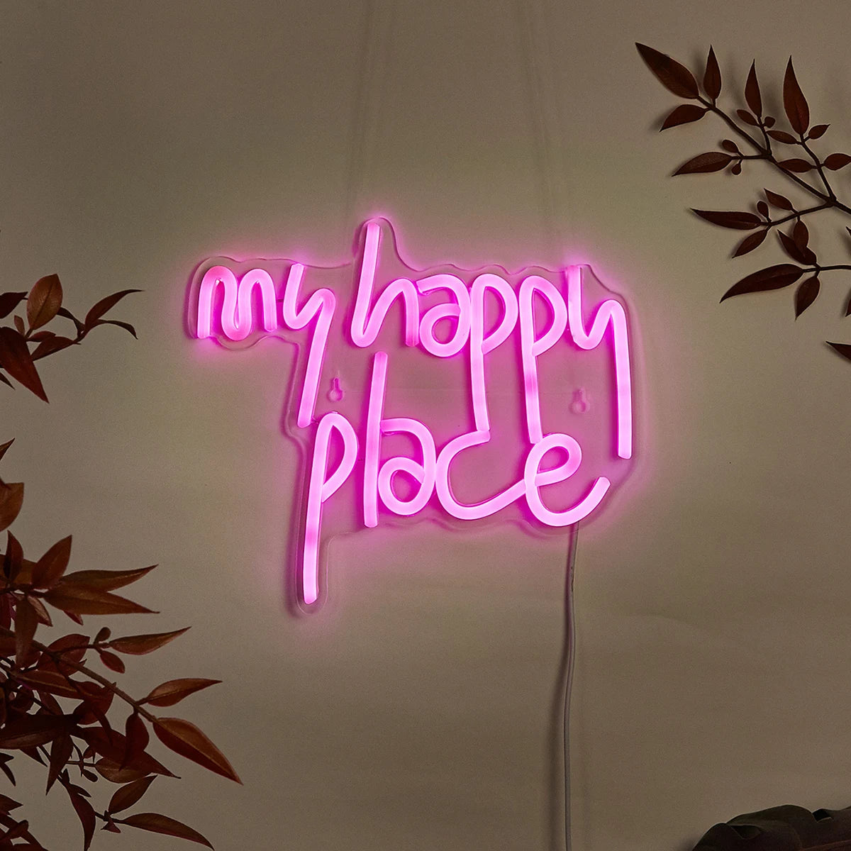 Pink neon sign spelling out My Happy Place mounted on a white wall with dark leaves in the background