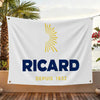 A white flag featuring a yellow sunburst graphic and the text RICARD DEPUIS 1932, displayed outdoors.