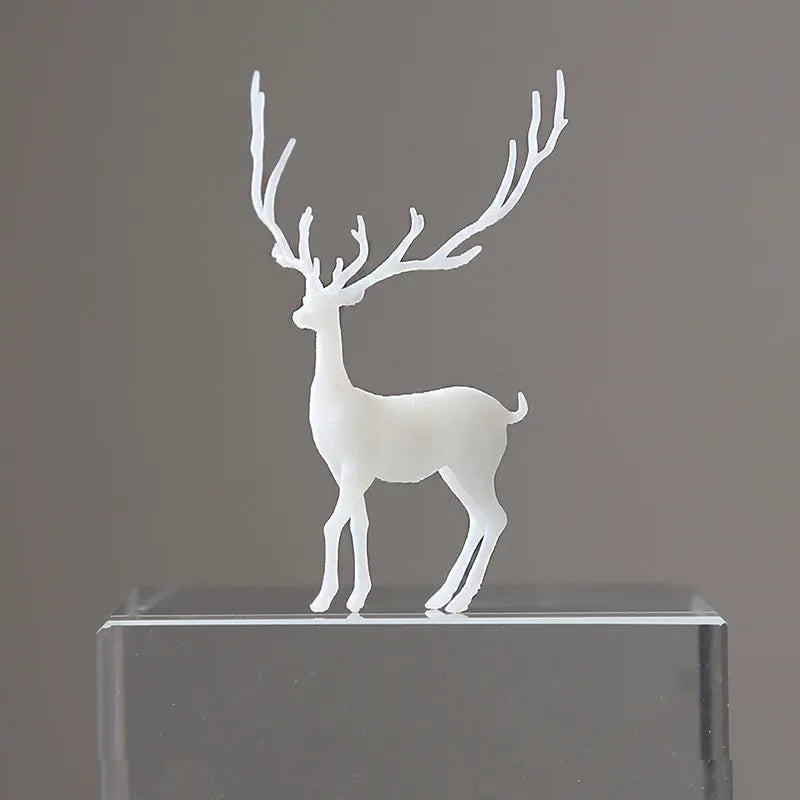 A white resin ornament of an elk deer with antlers standing on a clear glass base.