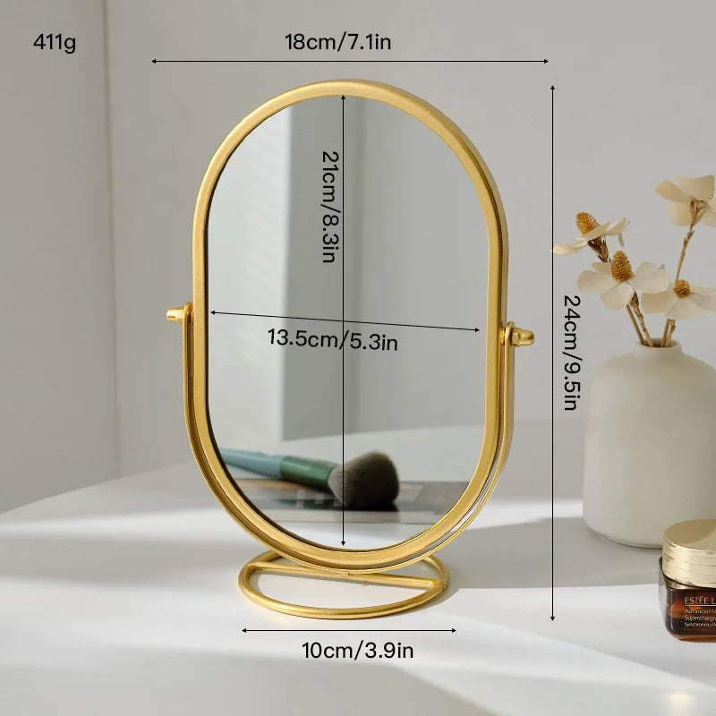 A gold-framed oval vanity mirror with a round base and a reflective surface.