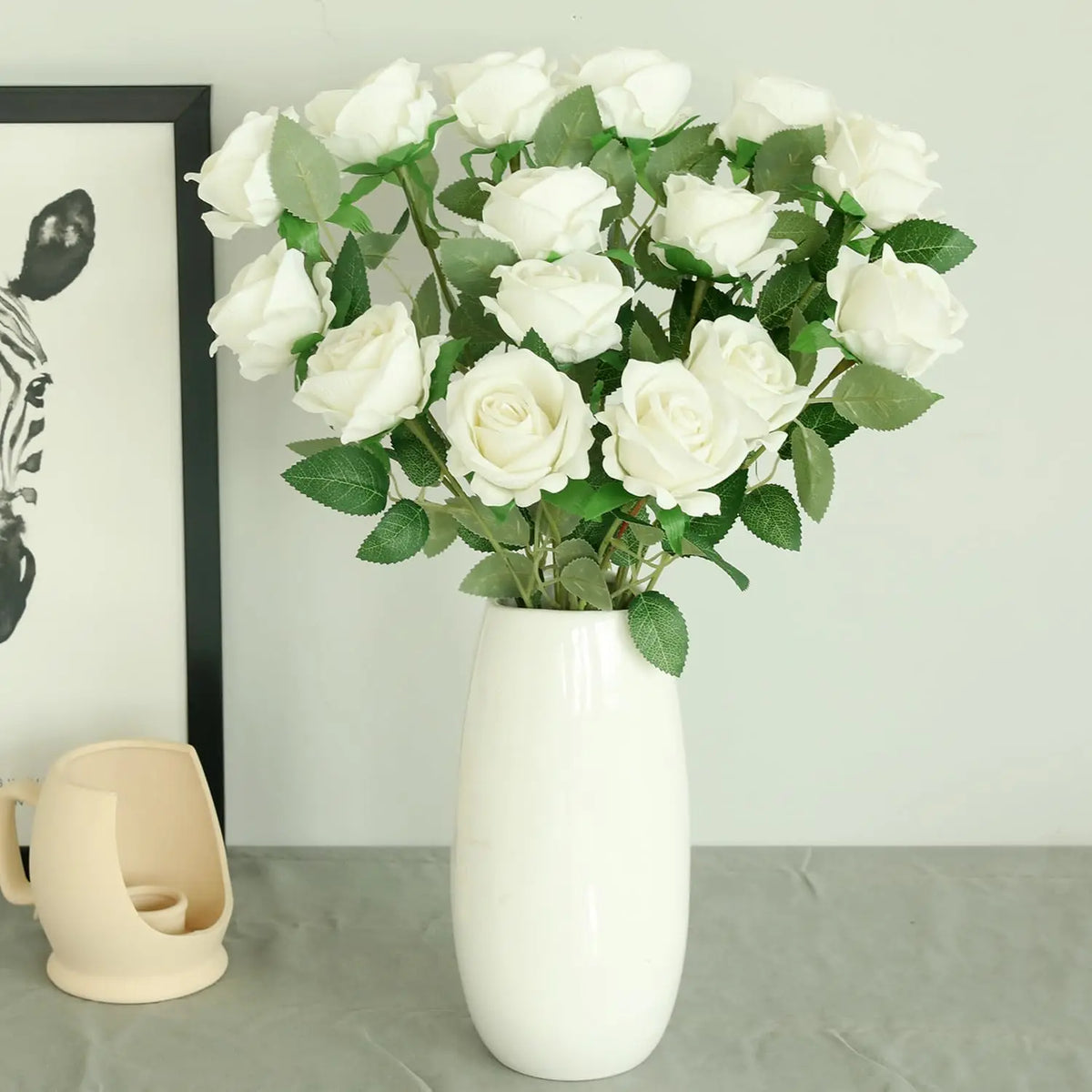 A white artificial silk rose bouquet in a ceramic vase displayed on a gray surface.