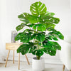 A vibrant artificial monstera plant with large green silk leaves in a white pot, displayed indoors.
