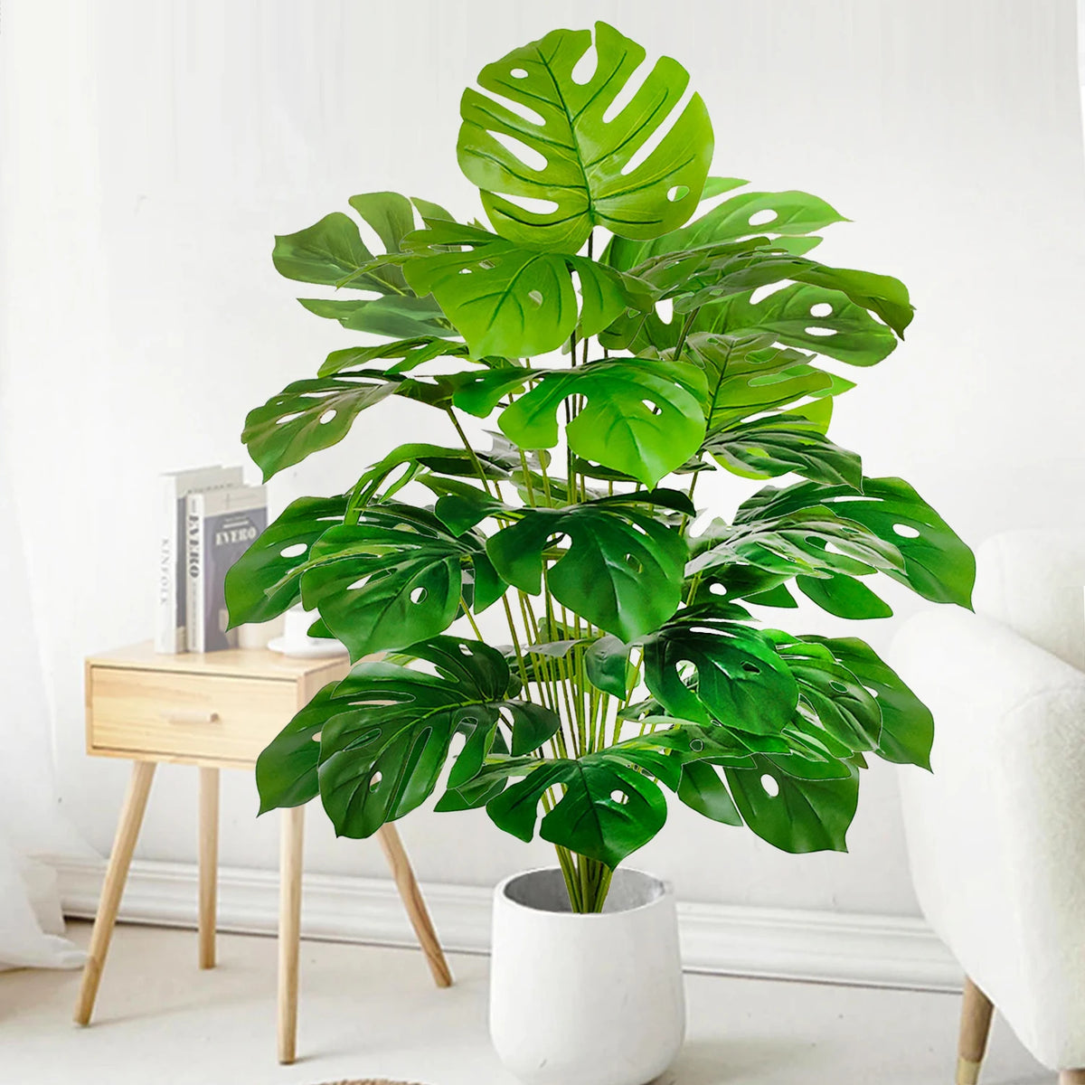 A vibrant artificial monstera plant with large green silk leaves in a white pot, displayed indoors.