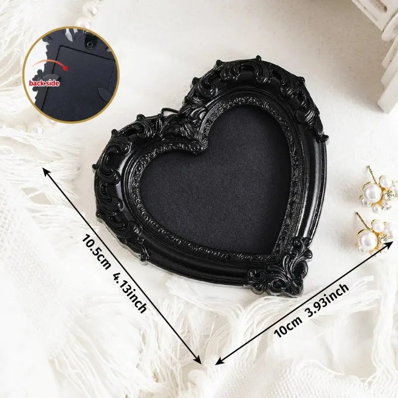 A black vintage resin heart-shaped picture frame with ornate detailing shown on a white fabric background.