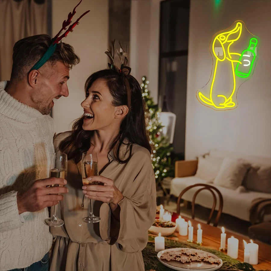 A woman and a man toast with drinks in a warmly lit room, near a neon sign of a dachshund.