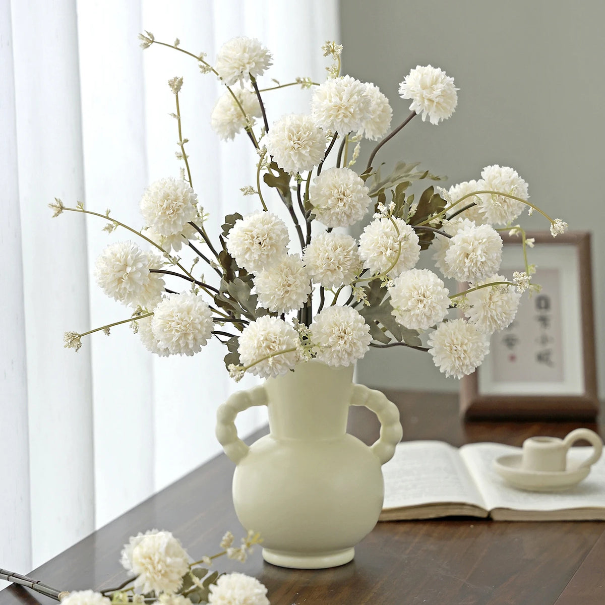 A bouquet of white silk chrysanthemum artificial flowers in a light ceramic vase on a wooden table.