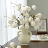 A bouquet of white silk chrysanthemum artificial flowers in a light ceramic vase on a wooden table.